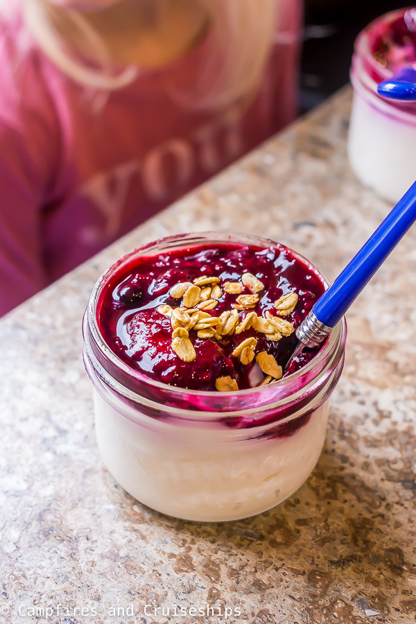 yogurt parfait in small jar with berry sauce and granola on top