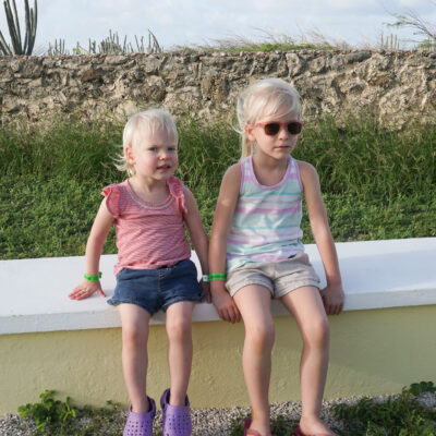 two young girls sitting on low wall in aruba
